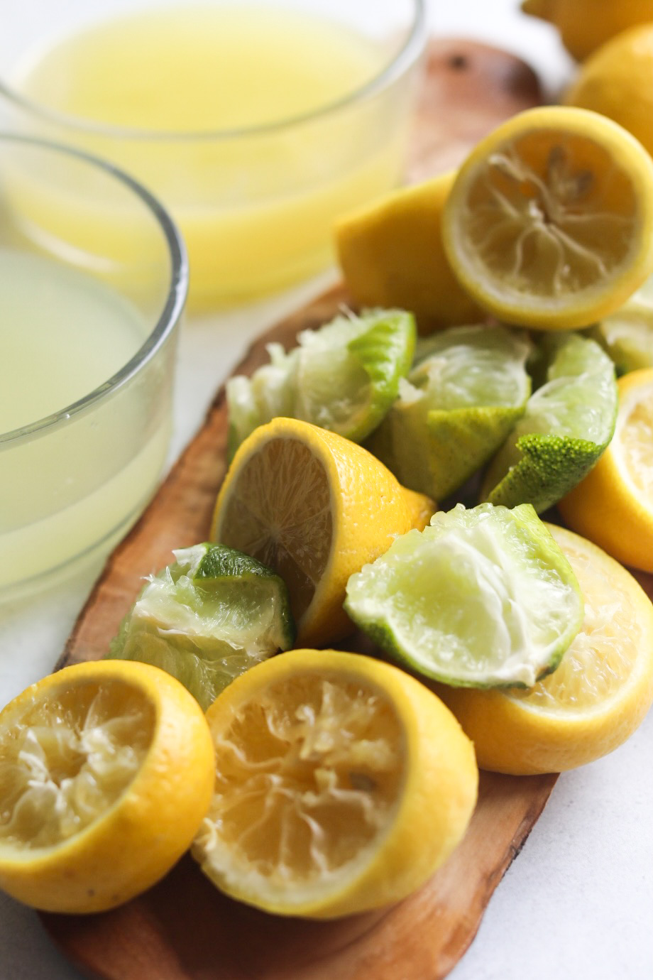 Used lemons and limes on a wood cutting board. Glass bowls filled with the juice from the lemons and limes on the left of the cutting board.