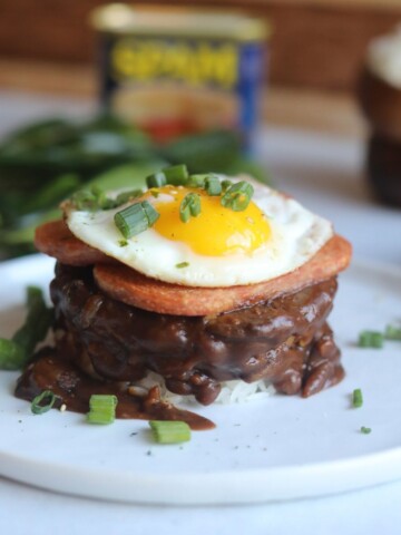 White rice topped with brown gravy, hamburger patty, topped with spam and a sunny side up egg.