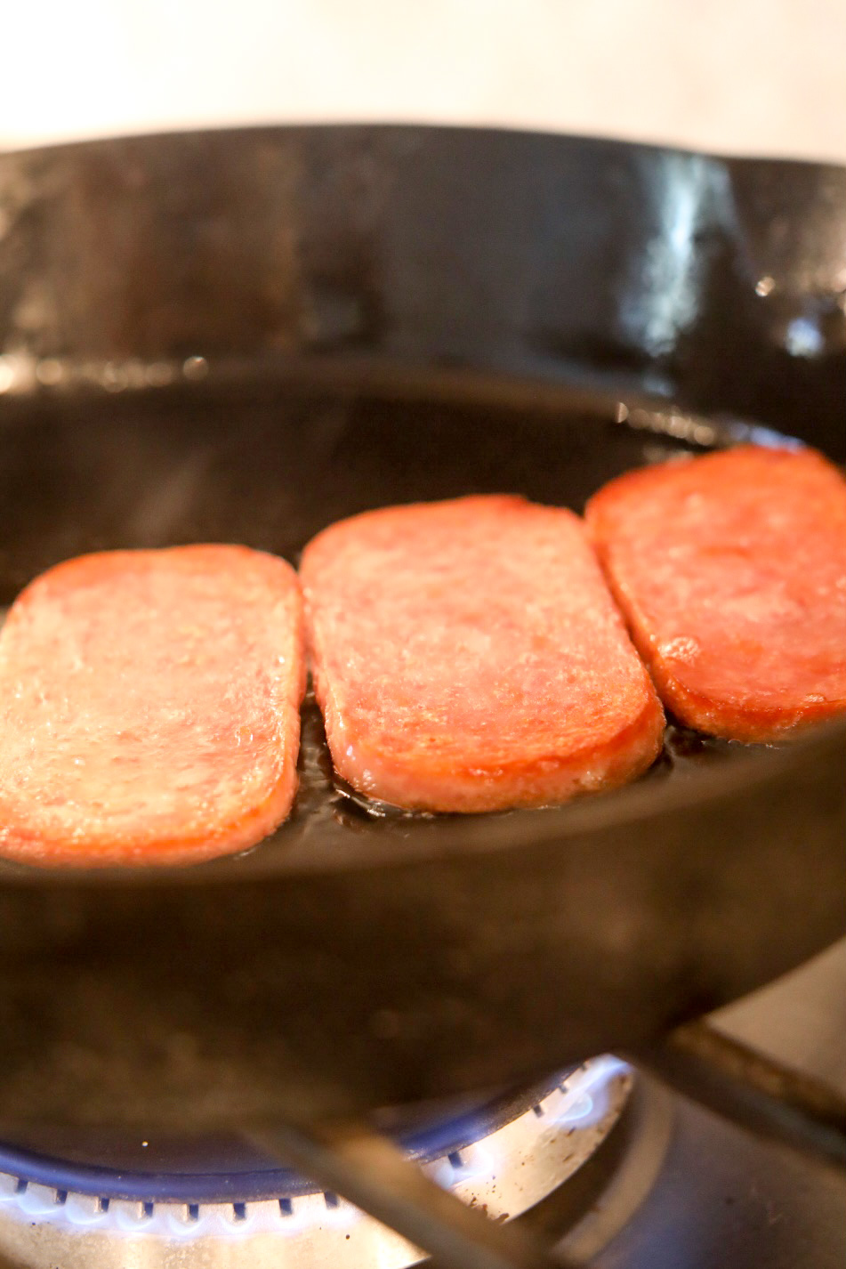 Three Slices of Spam in a black cast iron skillet.