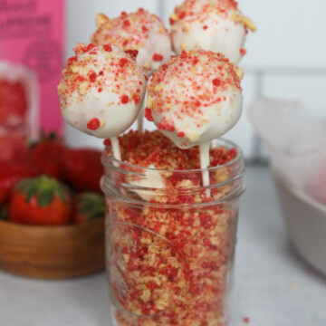 Strawberry Cake Pops in a short glass mason jar. Strawberry crunch is filled inside mason jar with four strawberry cake pops.