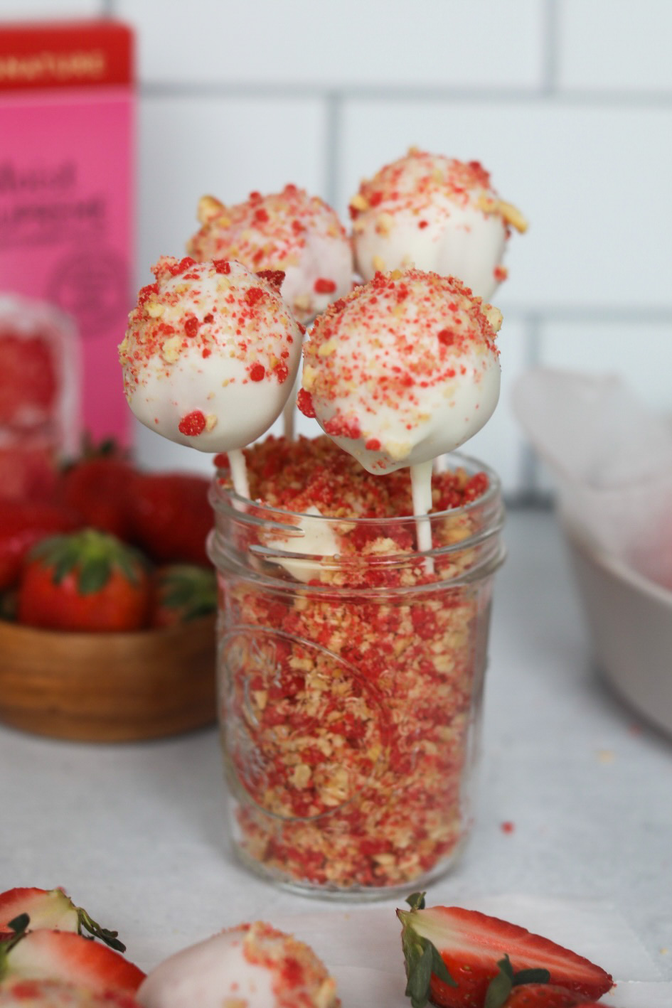 Strawberry Cake Pops in a short glass mason jar. Strawberry crunch is filled inside mason jar with four strawberry cake pops.