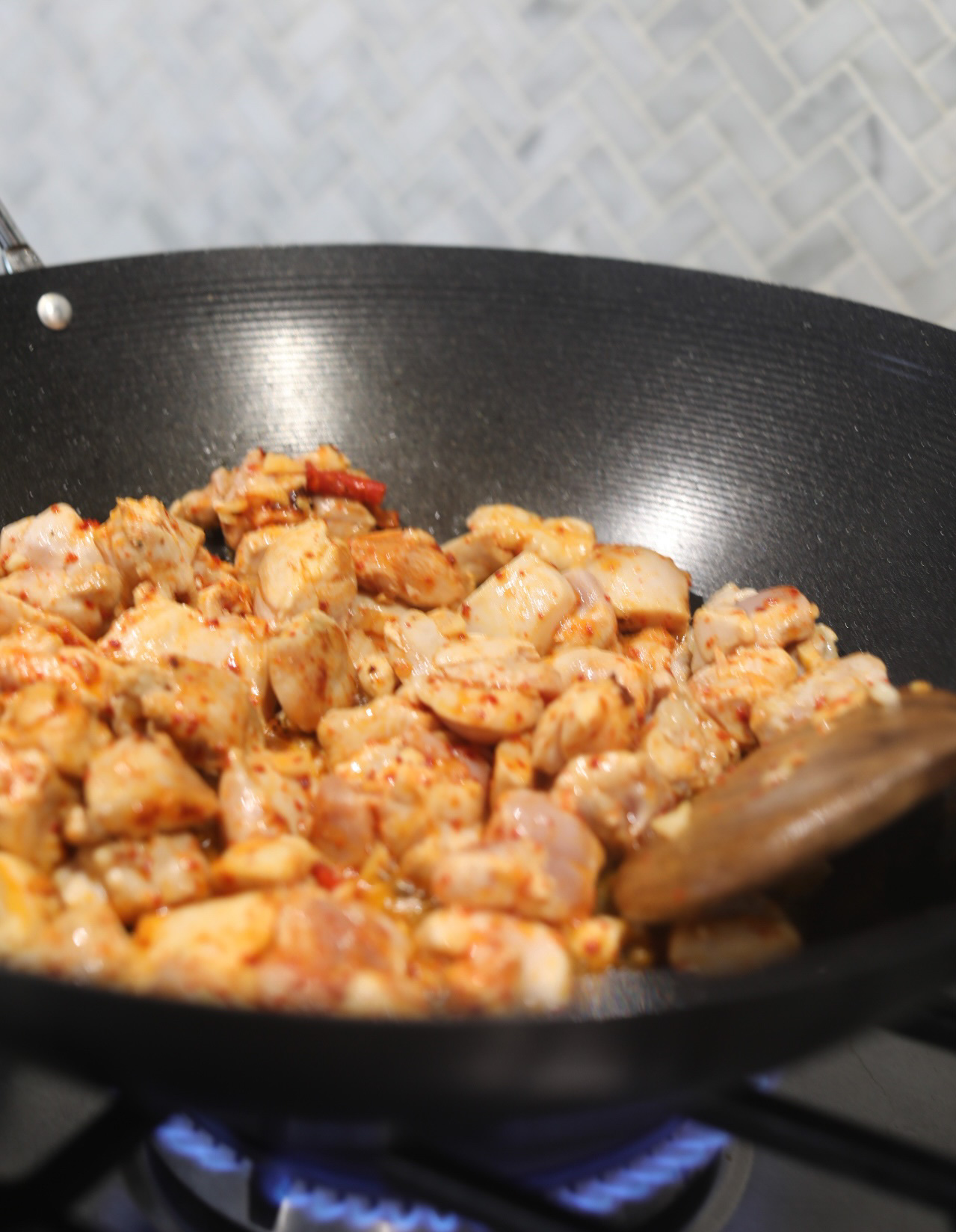 Chicken thighs cooking in a black wok with a wooden spoon.