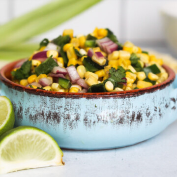 Chipotle copycat corn salsa in a blue serving dish with cut limes and ears of corn for styling purposes.