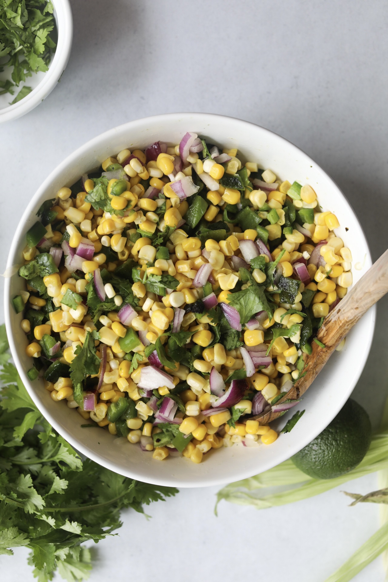 Corn salsa mixed in a white bowl with a wooden spoon.