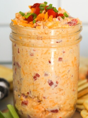 Pimento cheese in a glass mason jar topped with extra cheddar cheese, pimento cheese and green onions.