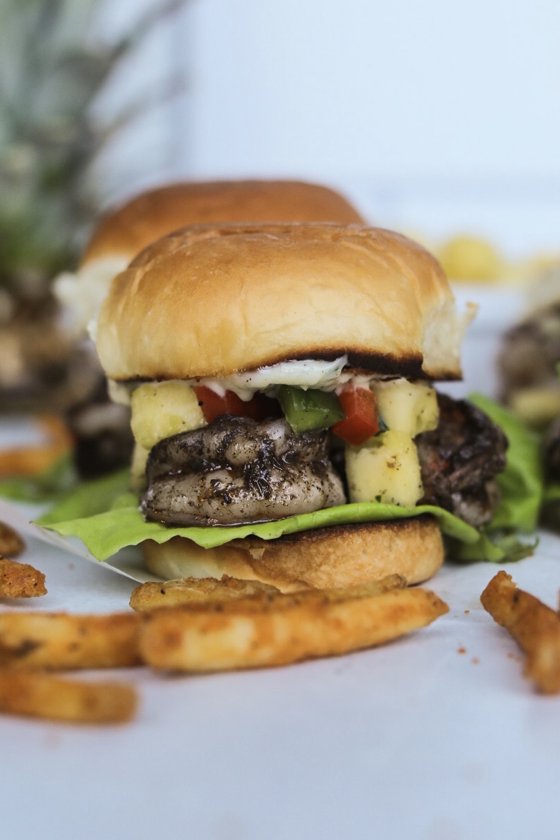 Jerk shrimp slider in focus with fries added for styling purposes. Pineapple added for styling purposes.