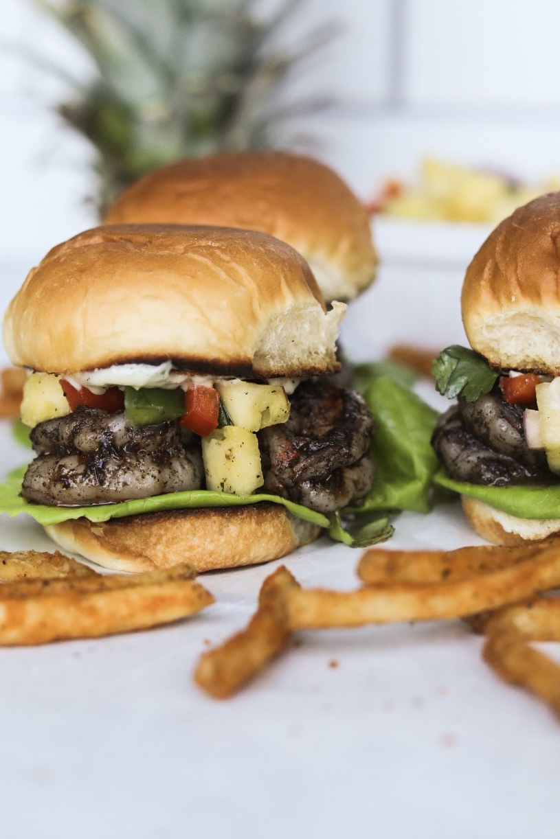 Finished recipe of jerk sliders styled with French fries and a pineapple added for styling purposes.