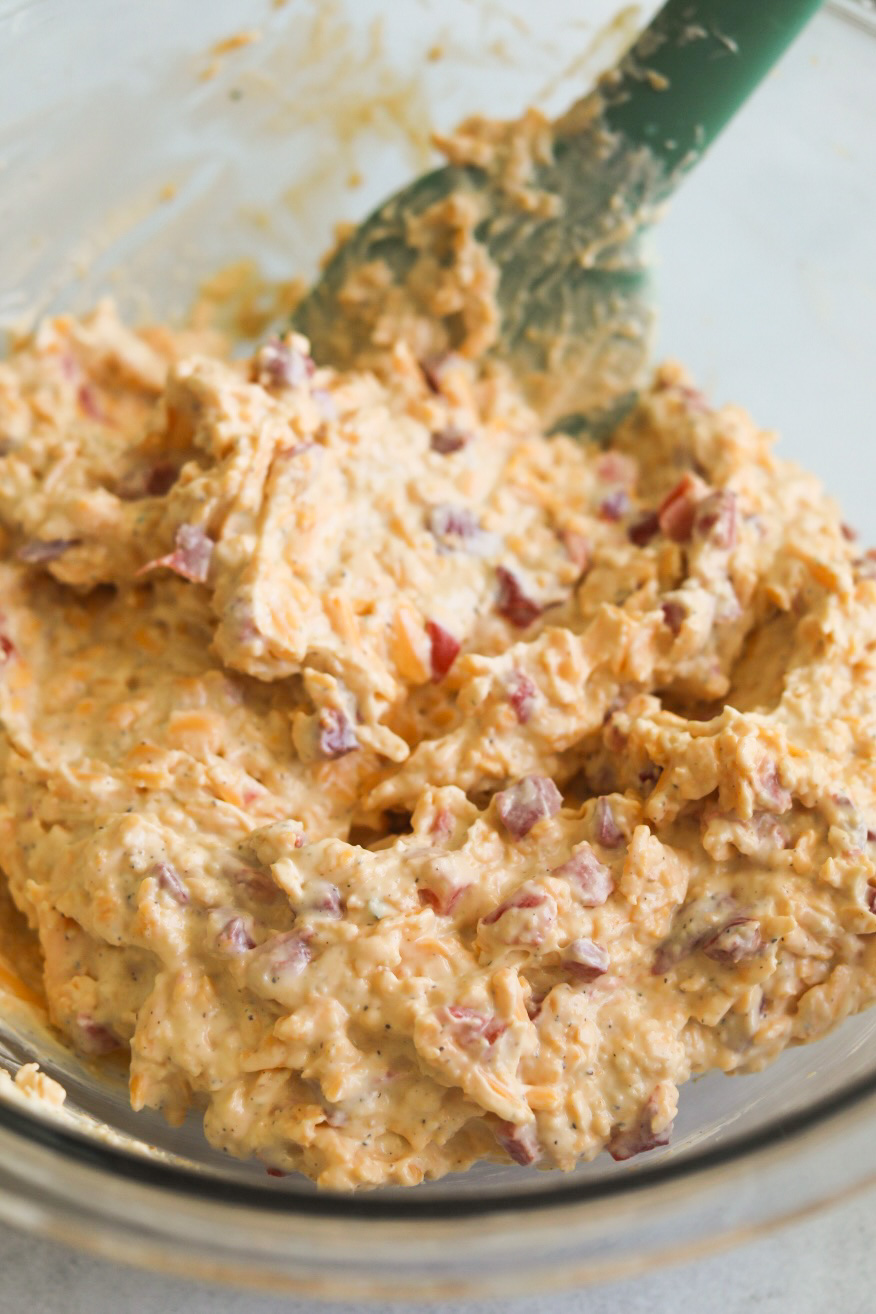 Mixed pimento cheese in a glass bowl with turquoise color spatula.