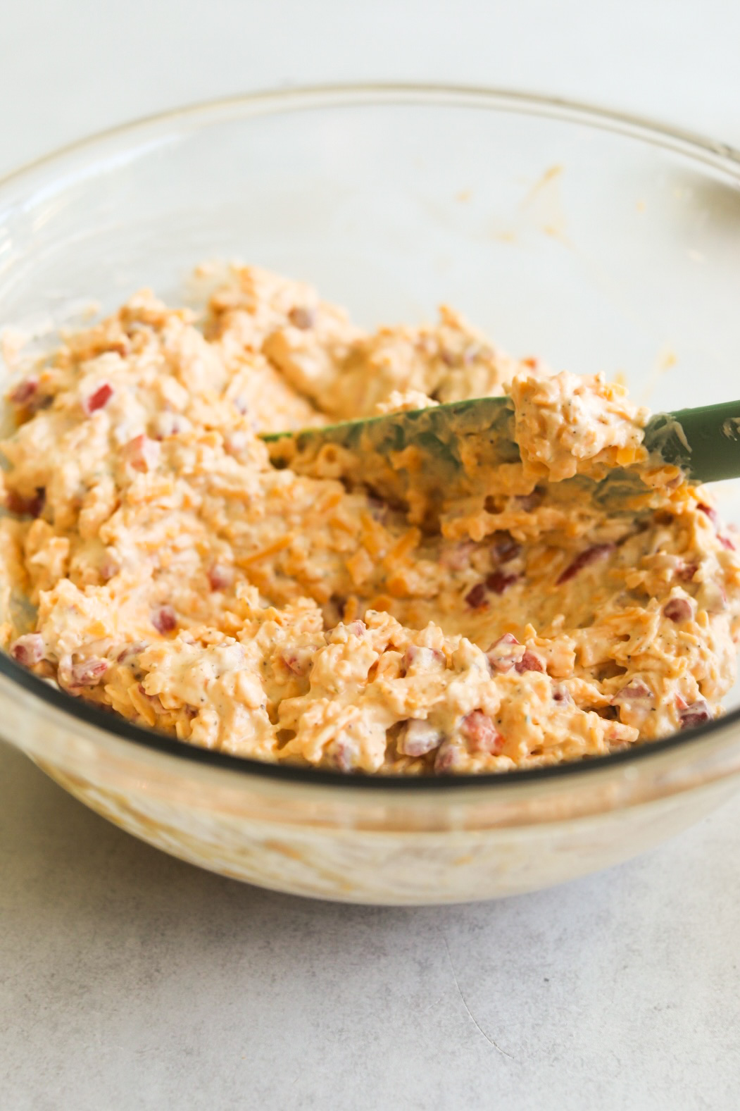 Mixed pimento cheese in a glass bowl with turquoise color spatula.