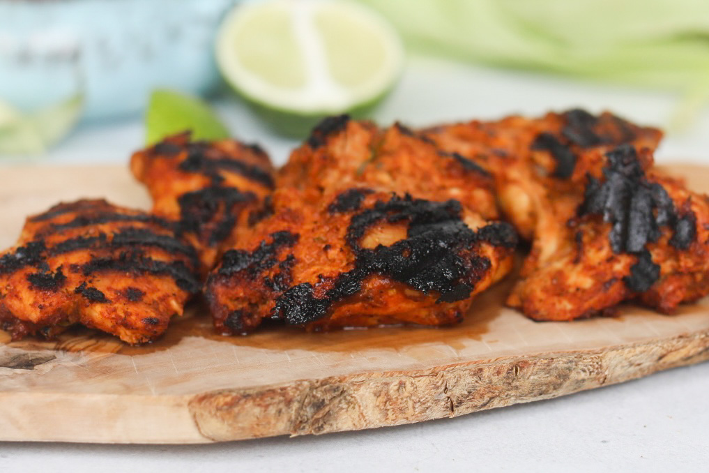 Pollo asado chicken cooked with char marks on a cutting board.