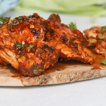 Pollo asado chicken thighs cooked drenched in red sauce on a cutting board garnished with chopped cilantro.