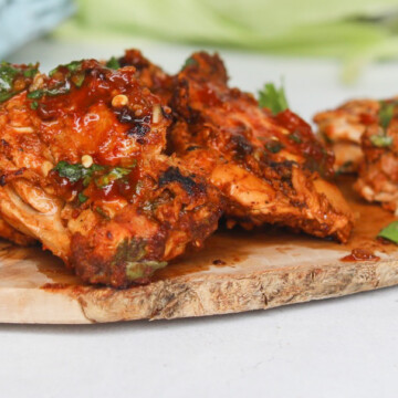 Pollo asado chicken thighs cooked drenched in red sauce on a cutting board garnished with chopped cilantro.