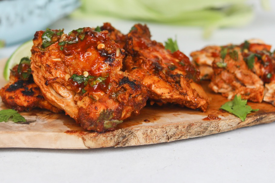 Pollo asado chicken thighs cooked drenched in red sauce on a cutting board garnished with chopped cilantro.