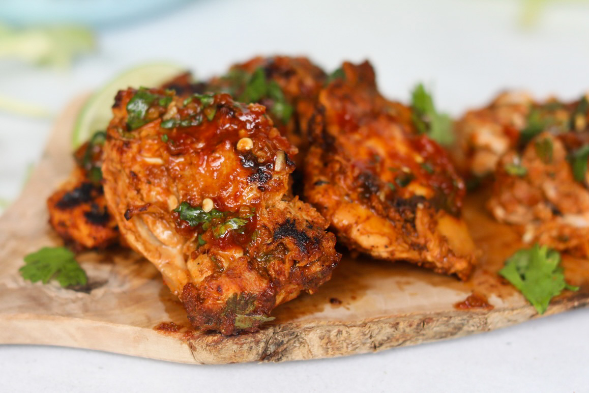 Pollo asado chicken thighs cooked drenched in red sauce on a cutting board garnished with chopped cilantro.