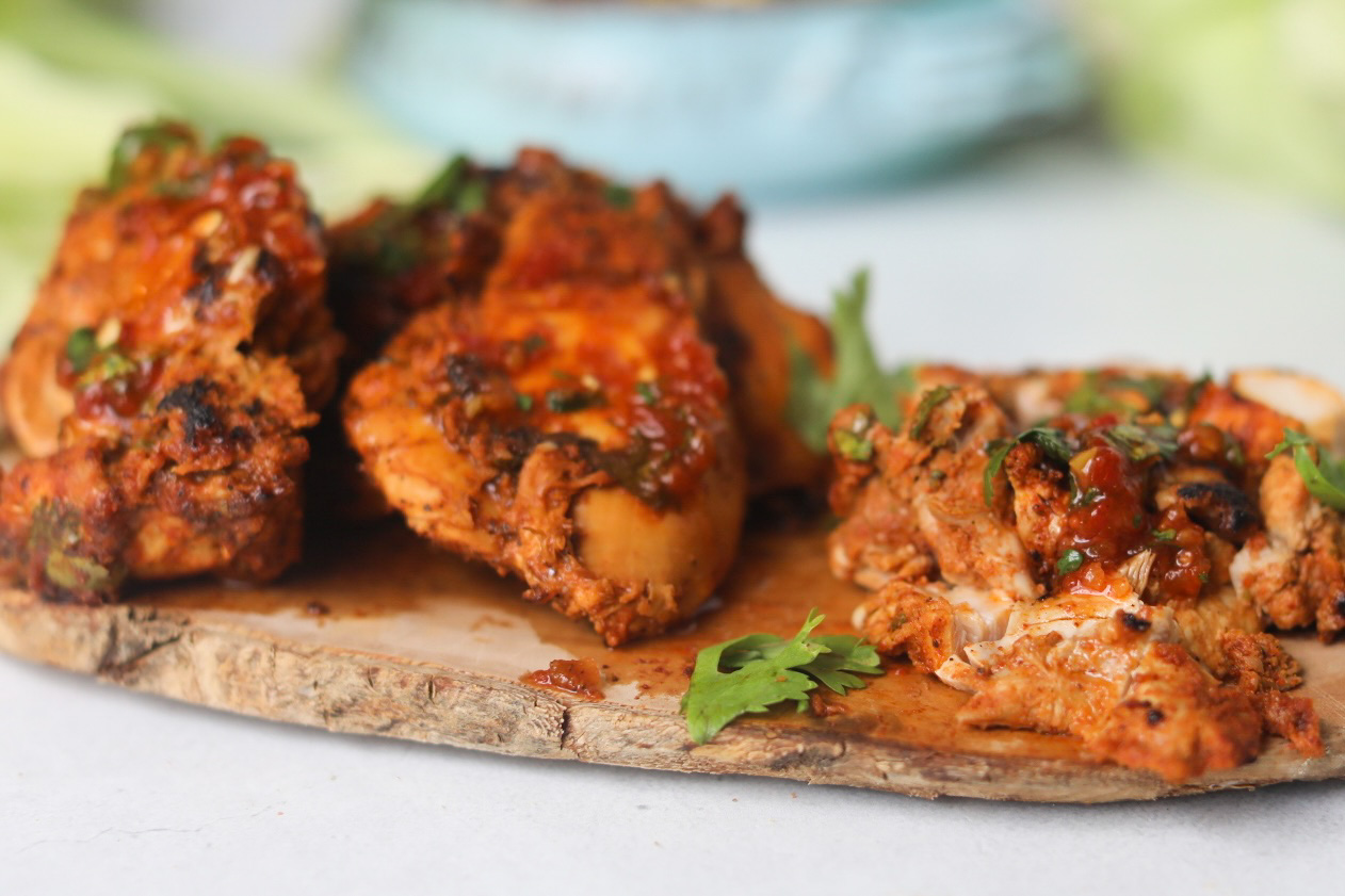 Finished pollo asado chicken thighs on a cutting board with chopped cilantro.