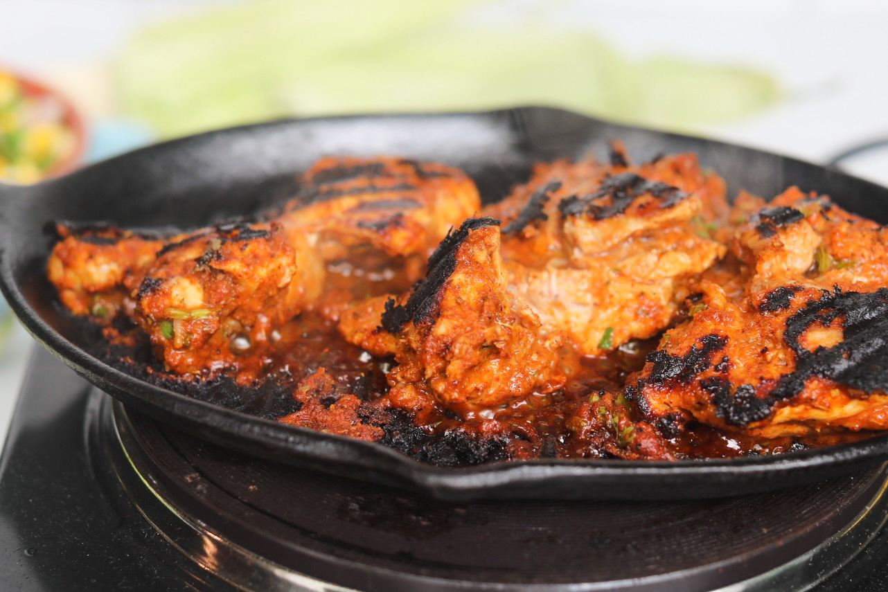 Pollo asado chicken thighs cooking in a black cast iron skillet.