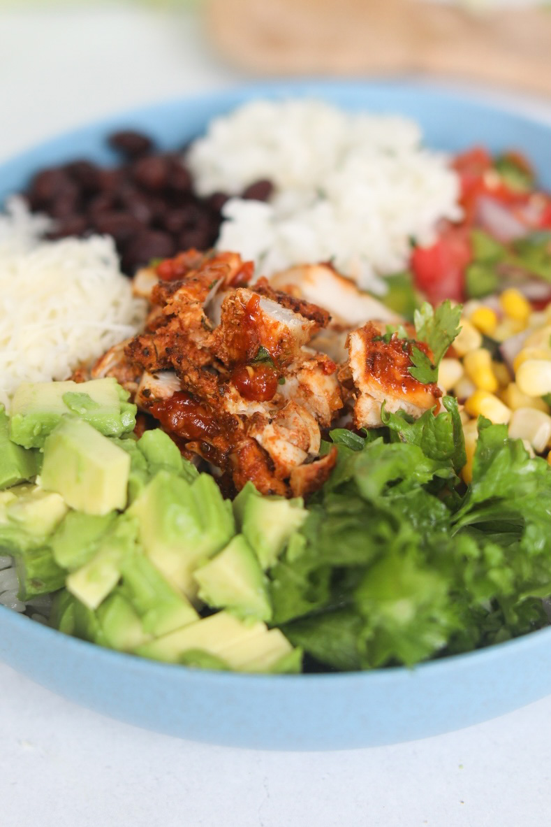 Chicken burrito bowl loaded with toppings and focus is on chopped pollo asado chicken.