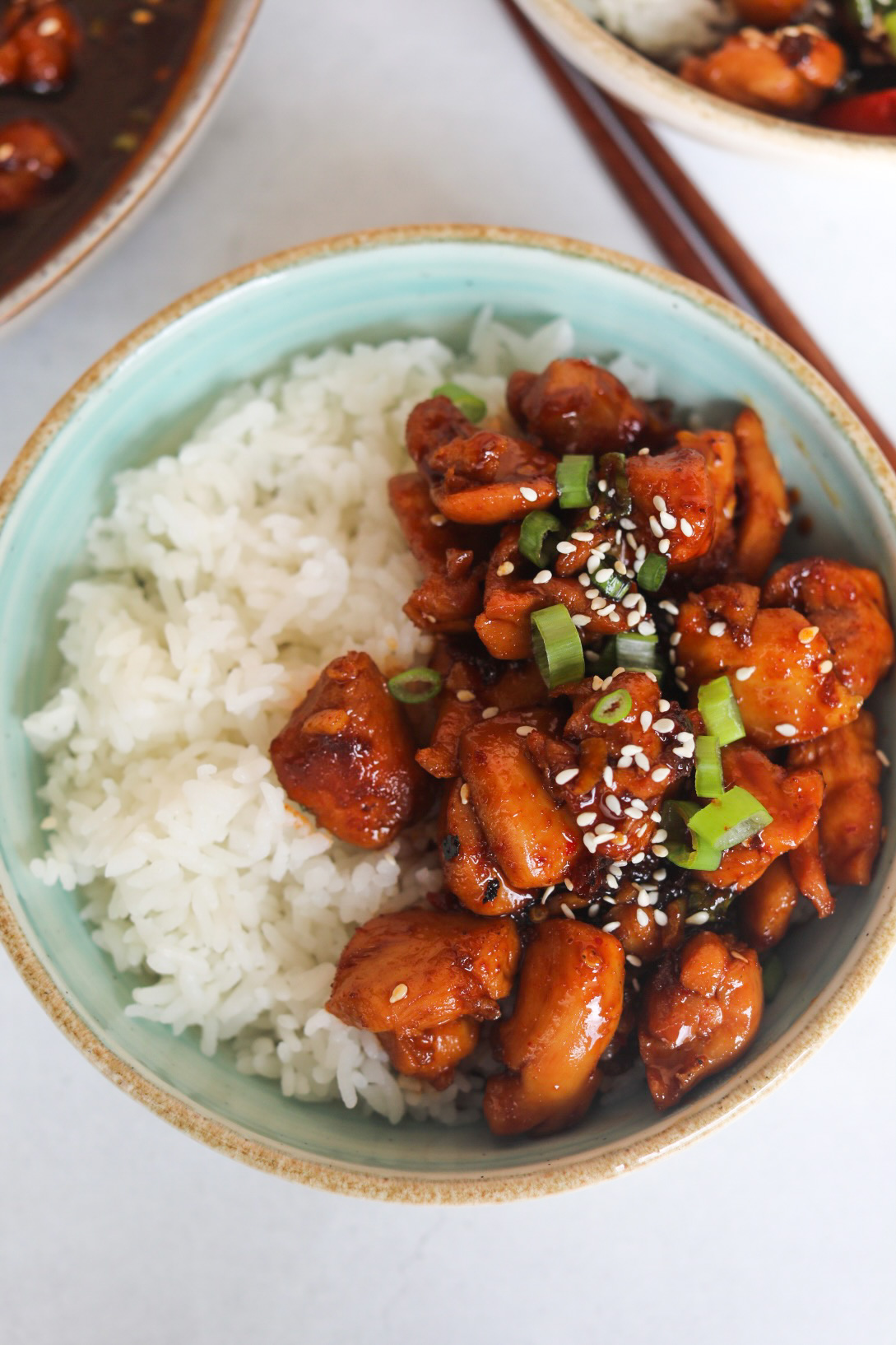 Spicy Chicken Teriyaki in a blue bowl with white rice topped with green onion and sesame seeds.
