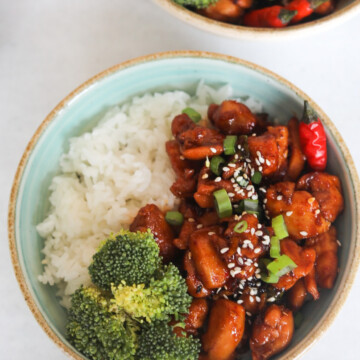 Spicy Chicken Teriyaki served in blue bowl with white rice and broccoli topped with green onion and sesame seeds.