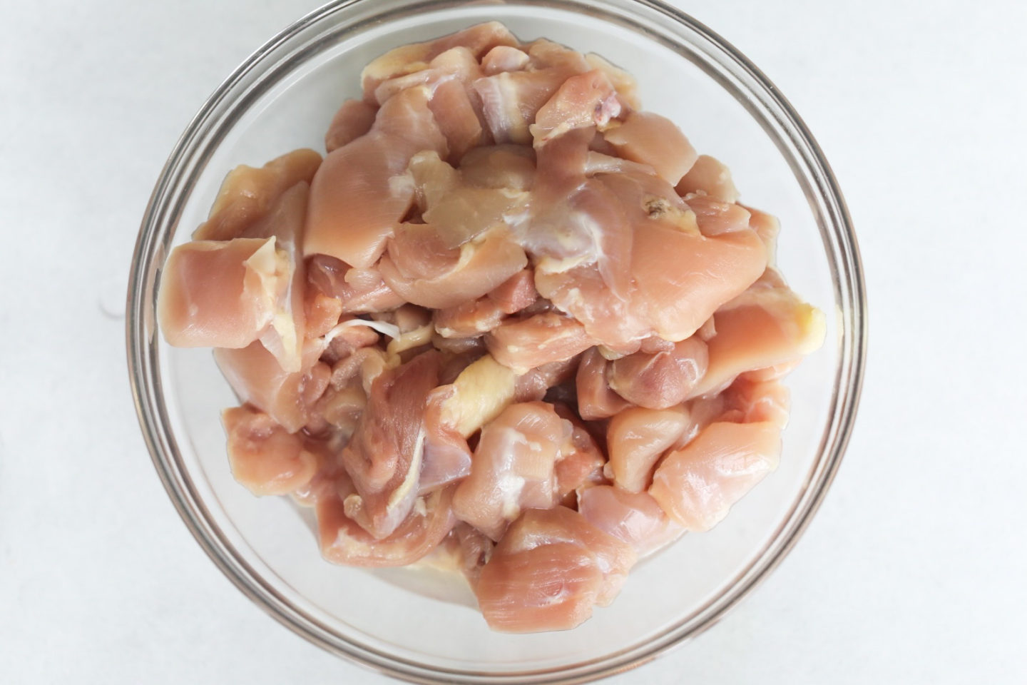 Uncooked Chicken Thighs in a clean bowl sliced in bite sized pieces for spicy chicken teriyaki recipe.