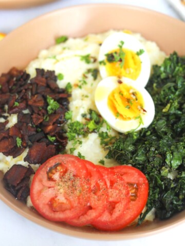 Grits and greens bowl topped with soft boiled egg, sliced tomato, kale and crunchy bacon.