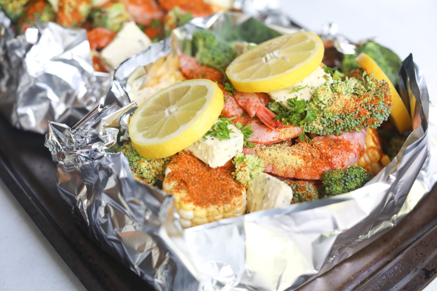 Prebaked shrimp boil foil packets in aluminium foil in a baking sheet ready to be baked!