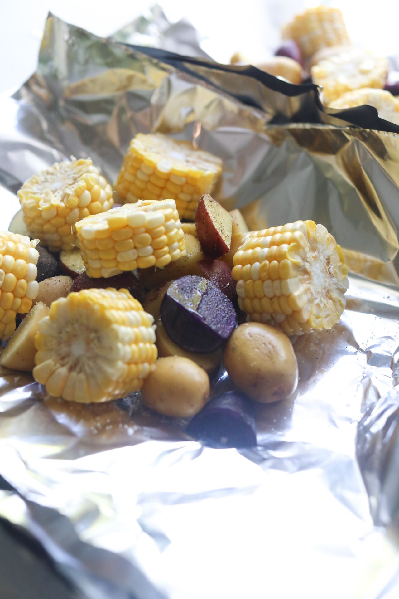 Aluminum foil filled chopped potatoes and sliced corn on the cobb for shrimp foil packets to be baked in the oven.