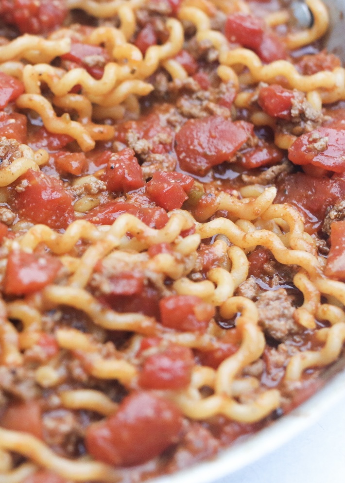 One pot taco spaghetti finished after noodles are cooked. In a large aluminum pan, cooked noodles, ground beef and tomatoes are simmering.