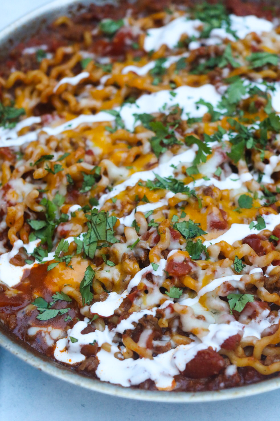 One pot taco spaghetti finished recipe in a metal pan with melted cheese, sour cream garnished with chopped cilantro.