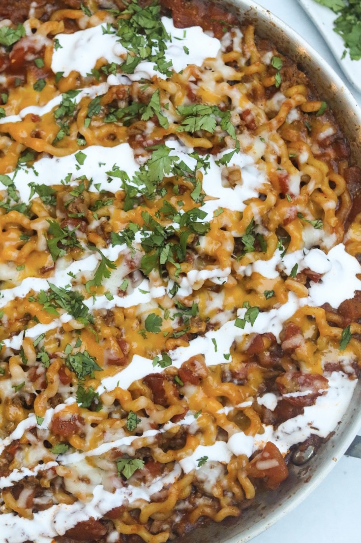 One pot taco spaghetti top down view with sour cream drizzle, melted cheese and chopped cilantro.