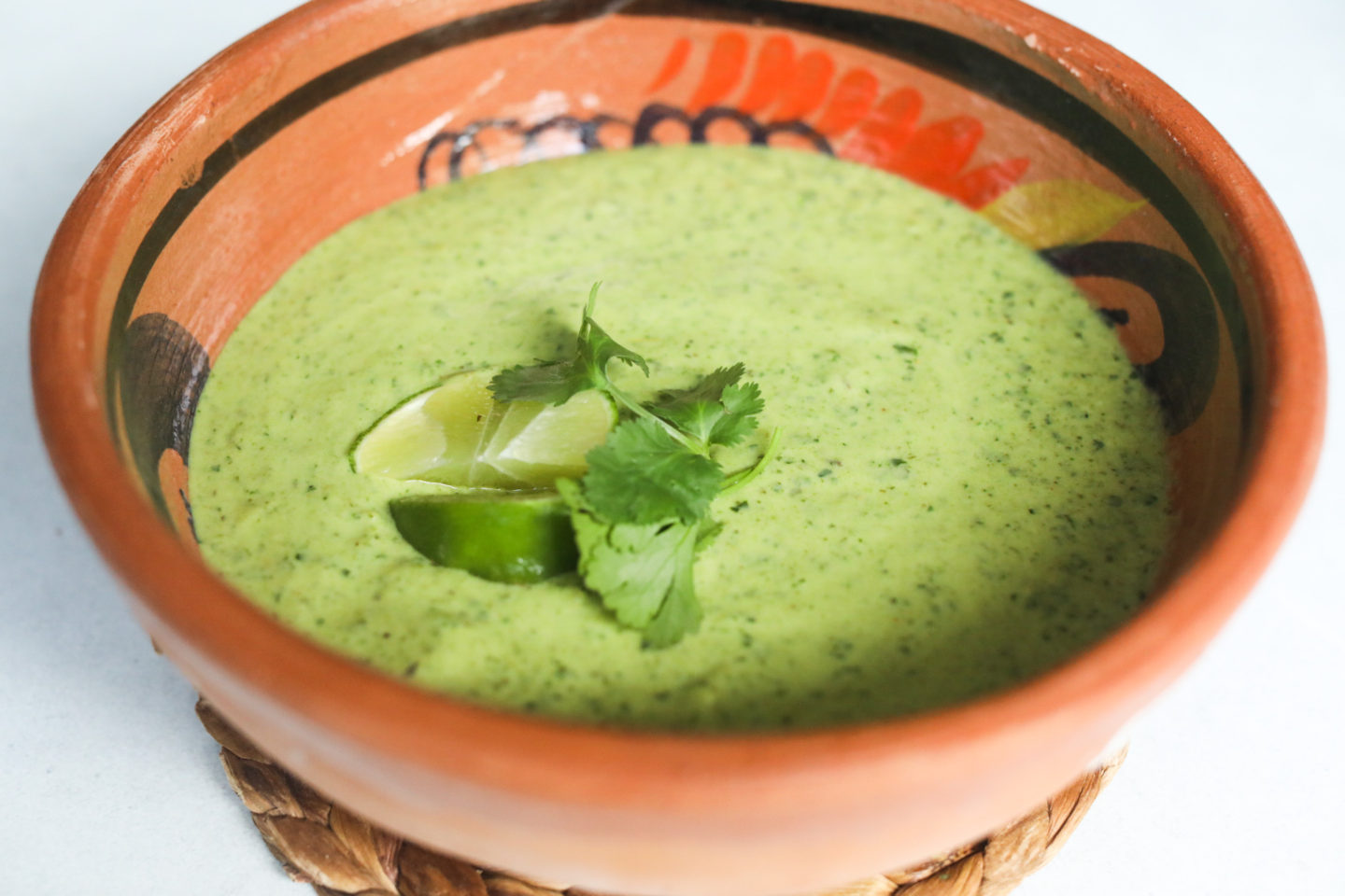 Poblano cream sauced in a clay/brown bowl topped with fresh cilantro and wedges of lime.