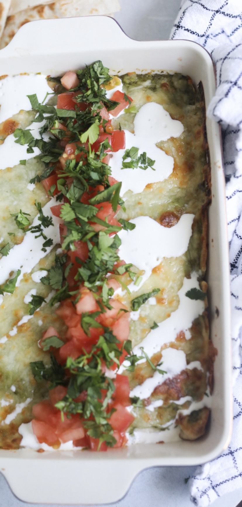 Chicken enchiladas with salsa verde. Recipe is complete in baking dish topped with diced tomatoes, cilantro and sour cream.