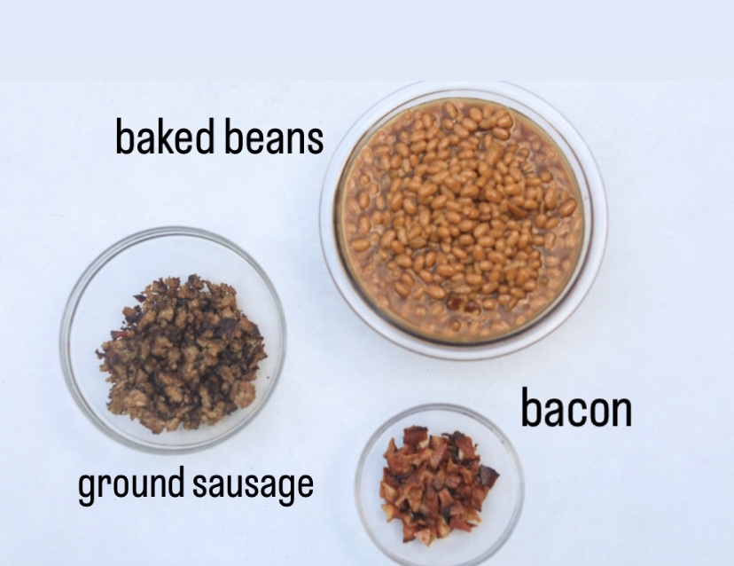 Sausage and baked bean casserole ingredients. In three glass bowls are baked beans, crumbled bacon and ground sausage.