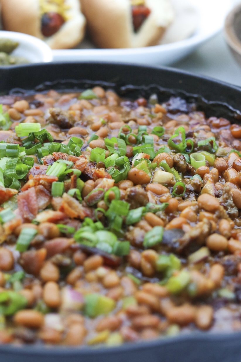 Sausage and Baked Bean Casserole in a black cast iron skillet with chicken skewer added for styling purposes. 