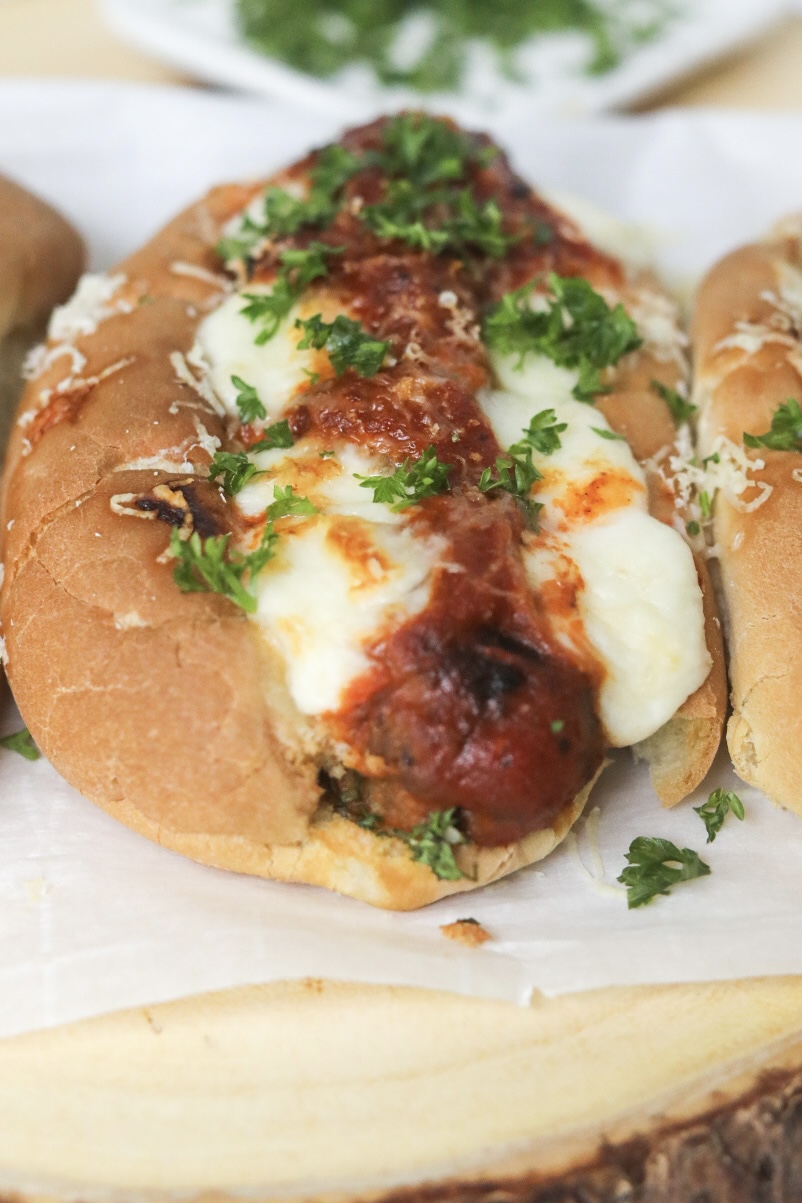 close up view of a meatball sandwich with gooey mozzarella cheese and fresh herbs