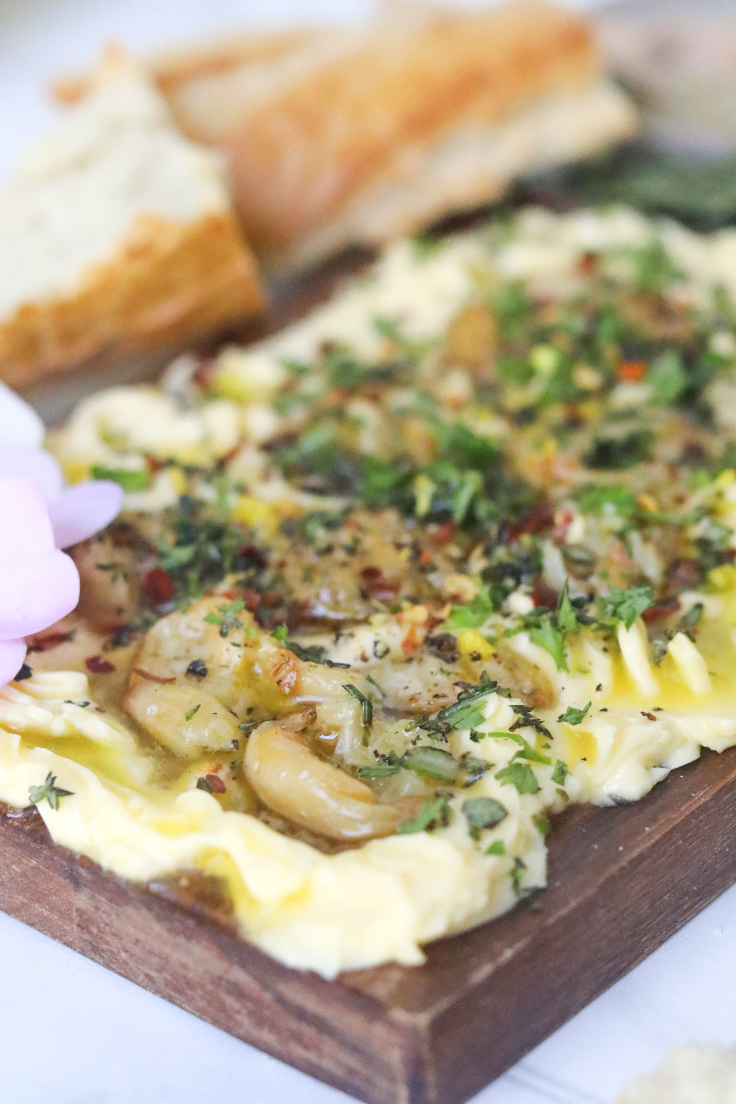 Side angled shot of butter board showing creamy butter and chunks of roasted garlic clovees.