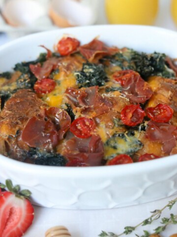 Breakfast Croissant Casserole with prosciutto in a white baking dish topped with cherry tomatoes.