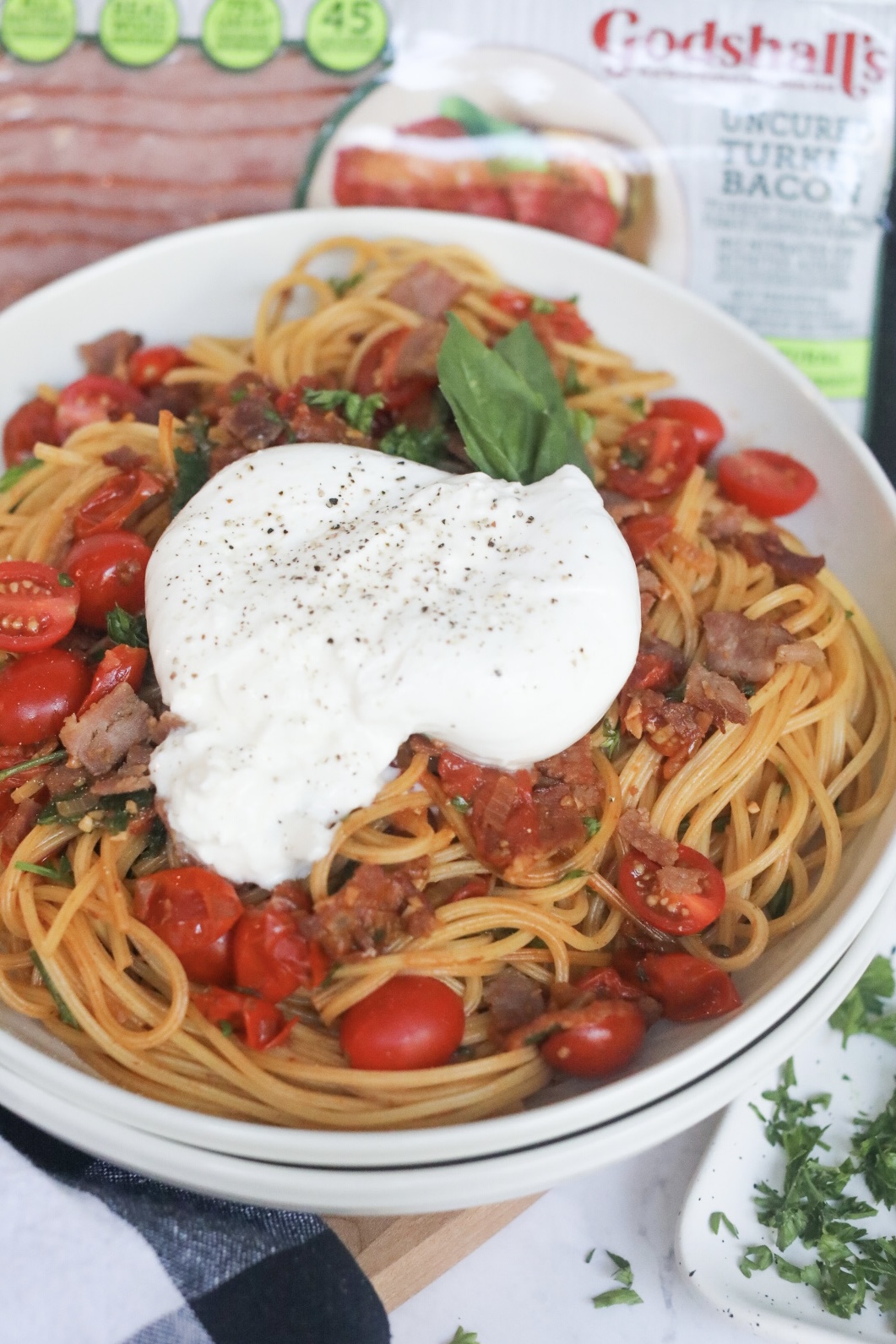 Complete recipe of burrata pasta with cherry tomatoes, bacon and fresh parsley, topped with fresh burrata.