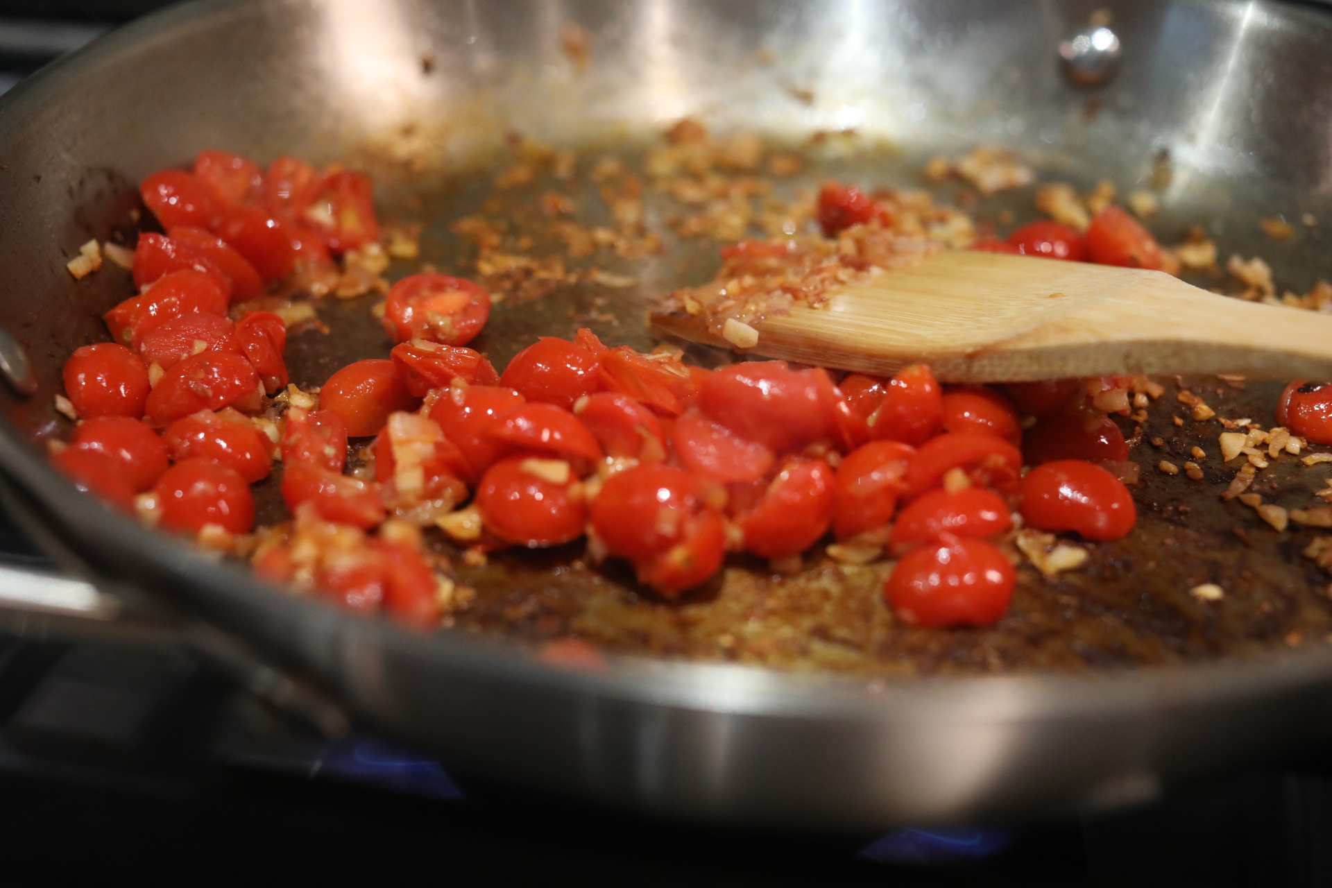 Cherry tomatoes with sauteed shallot and garlic sautéing in a metal pan with wooden spoon.