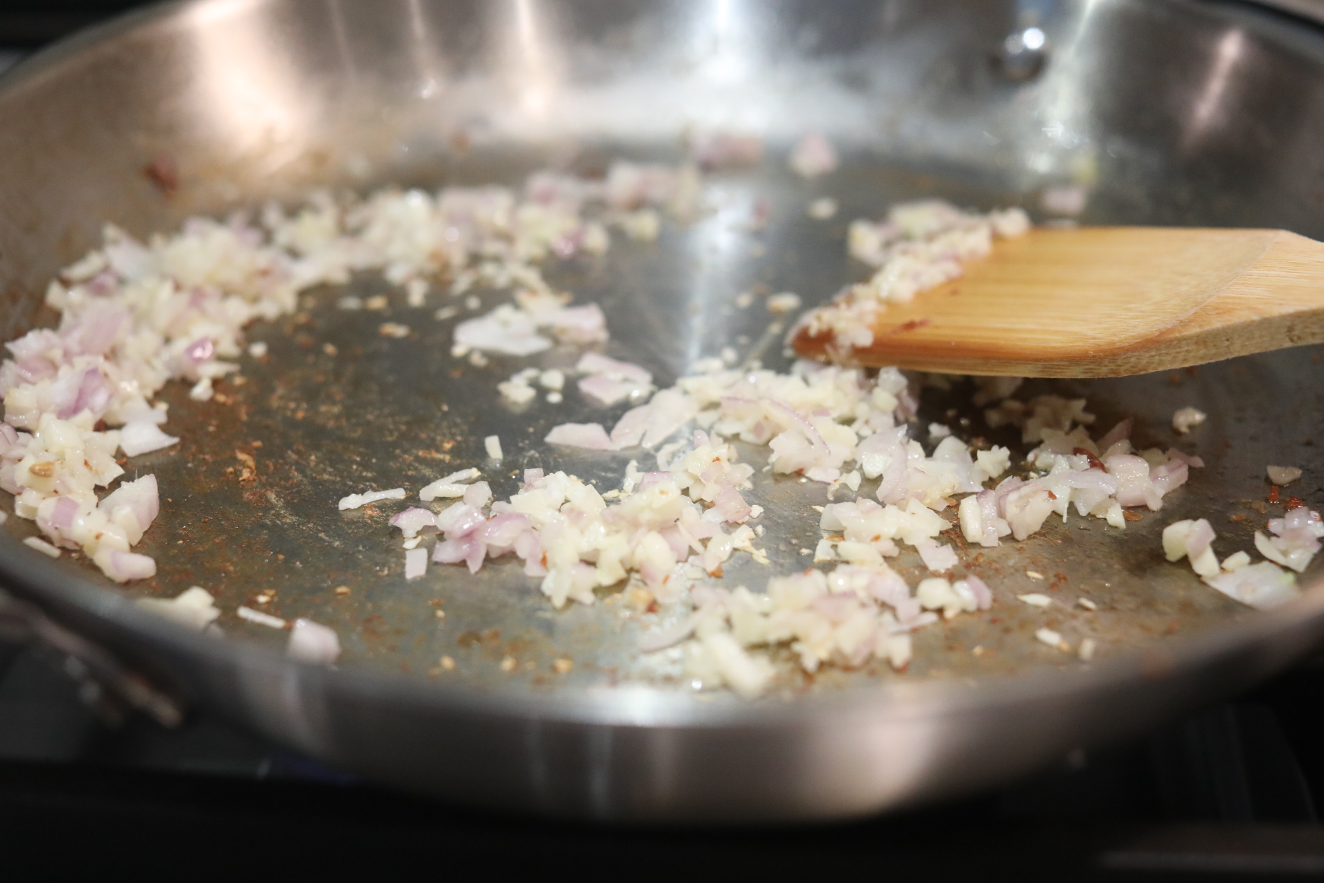 Shallot and garlic sautéing in metal pan with wooden spoon.