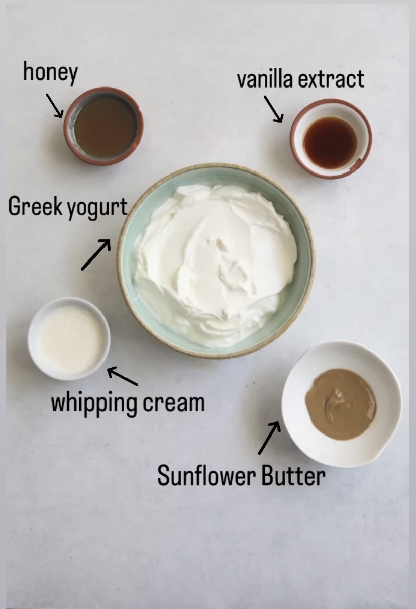 Whipped yogurt ingredients in a flat lay in various sized bowls. Large bowl of Greek yogurt, small bowls of vanilla extract, whipping cream, honey and sunflower butter.