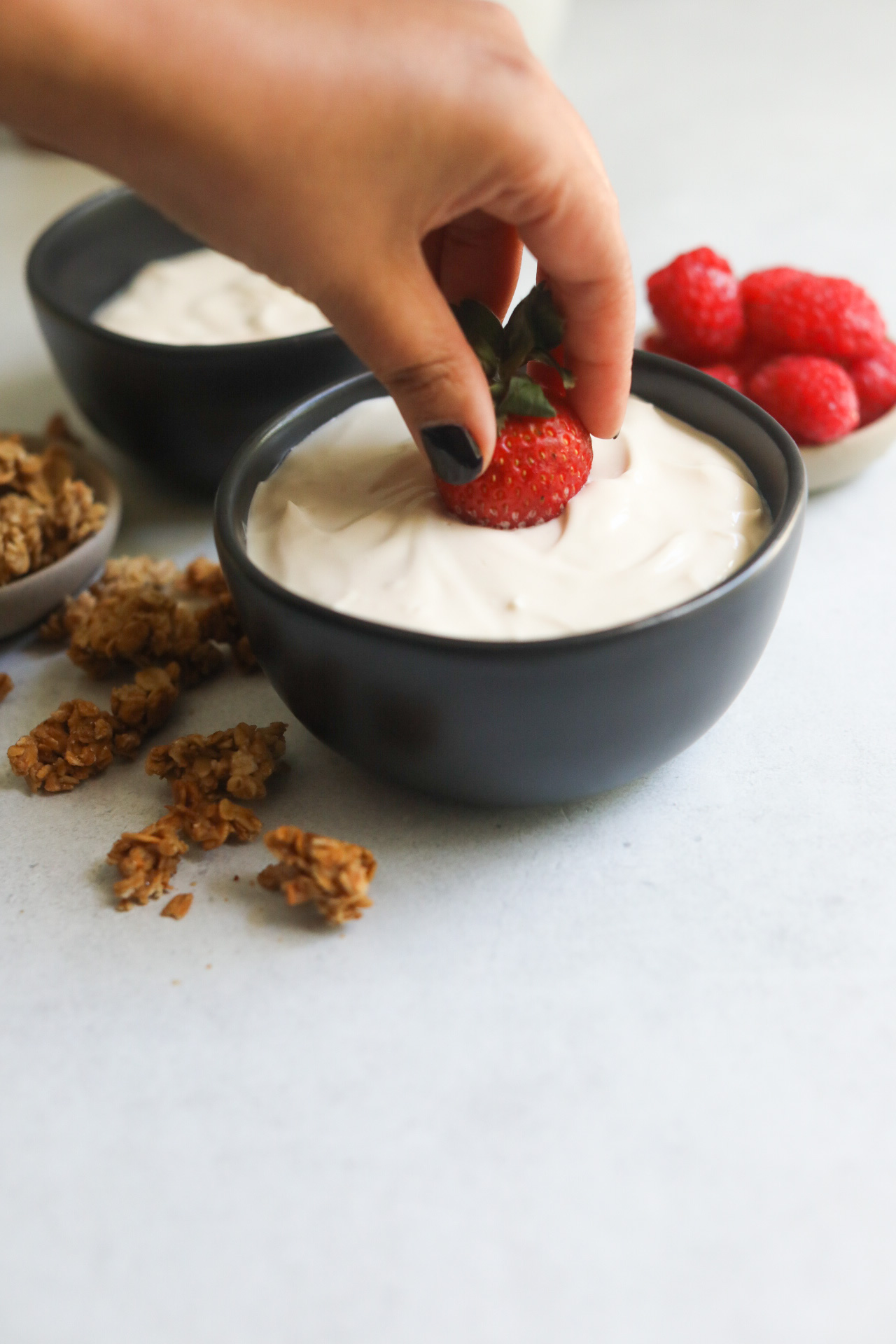 Hand dipped entirely into whipped yogurt to show as dipping sauce. Crumbled granola with small bowl of raspberries.
