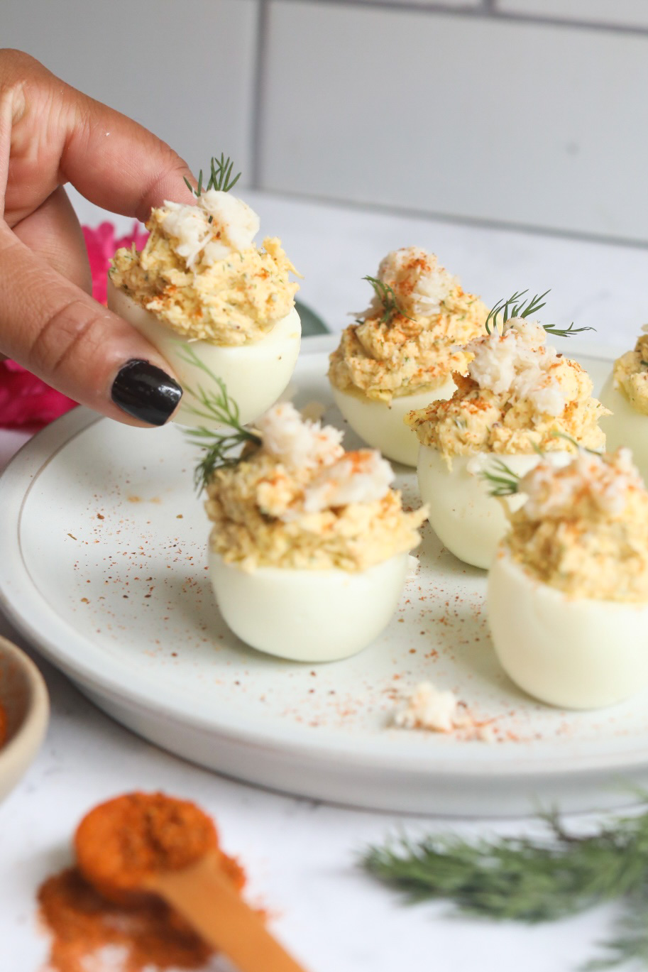 a hand holding one crab deviled egg from a platter