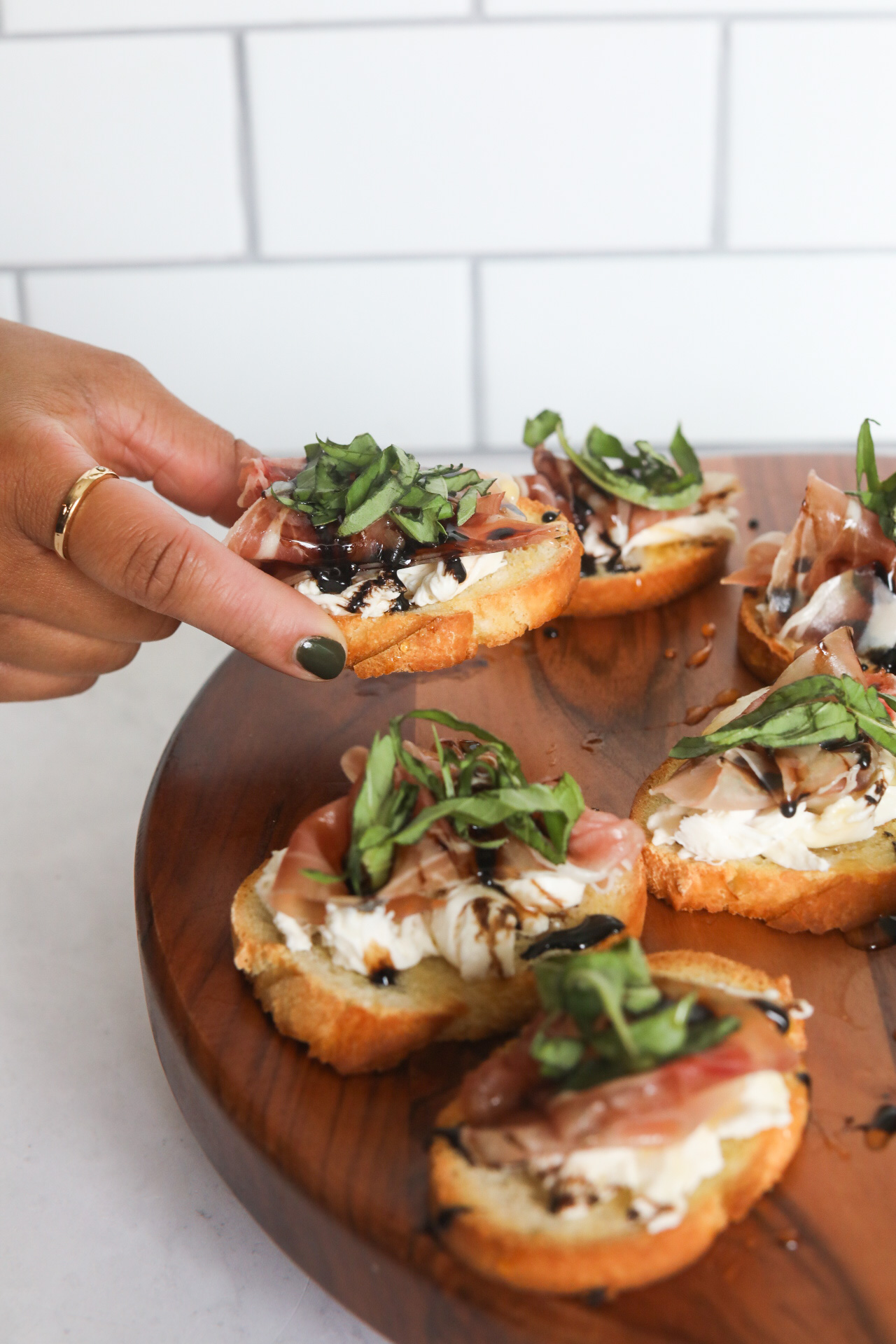 Crostini with Prosciutto with left hand picking up toast point from the wooden charcuterie board.