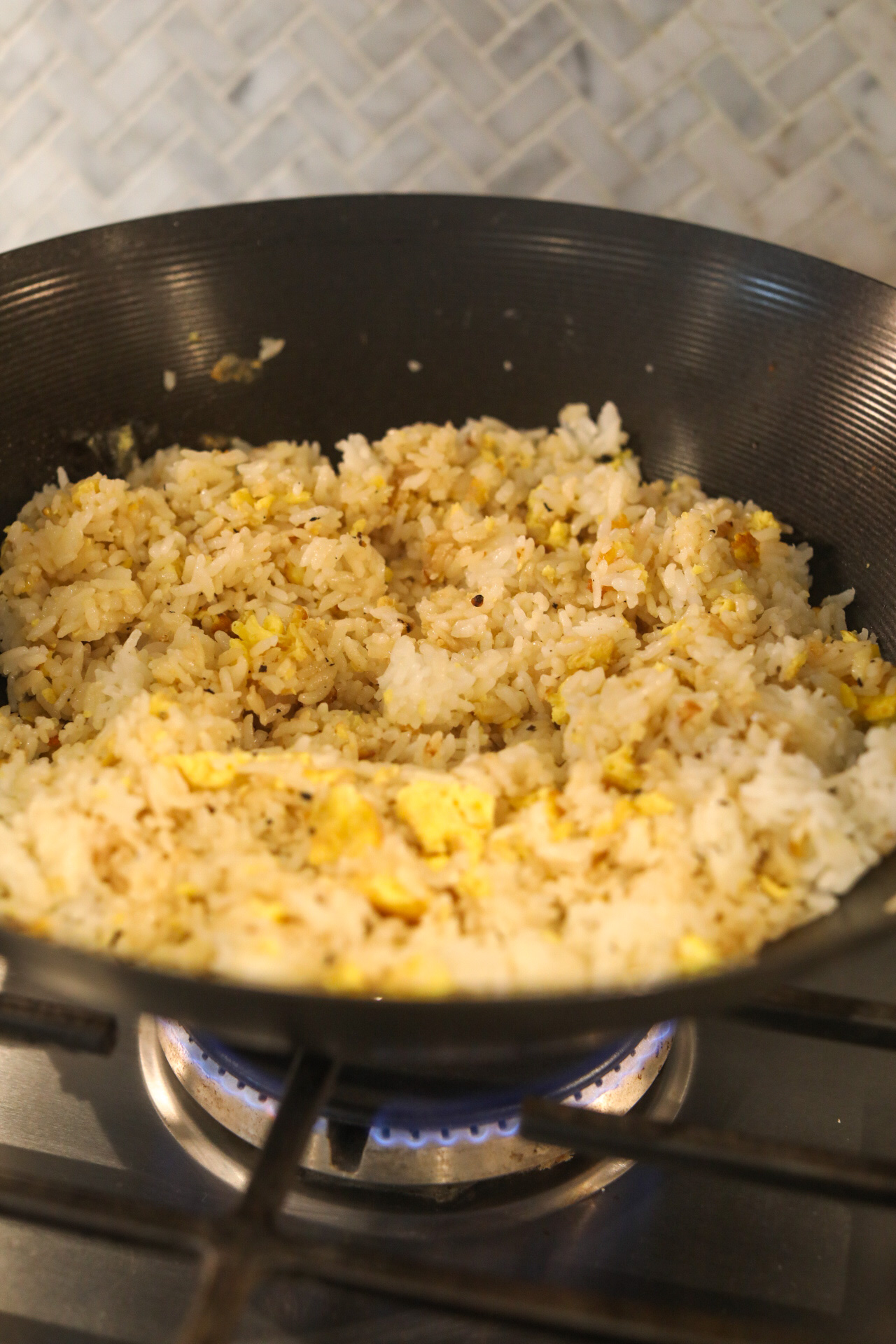 Sticky rice and scrambled eggs with shallot, garlic and ginger mix in black wok.