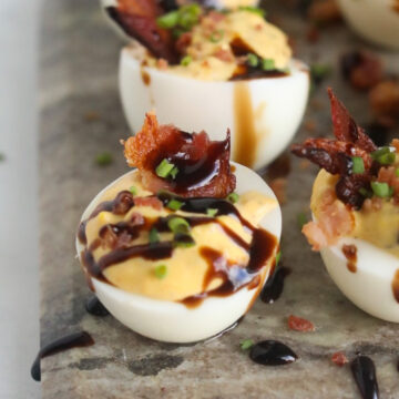 Southern Bacon Deviled Eggs with Balsamic Glaze plated on top of a marble slab.