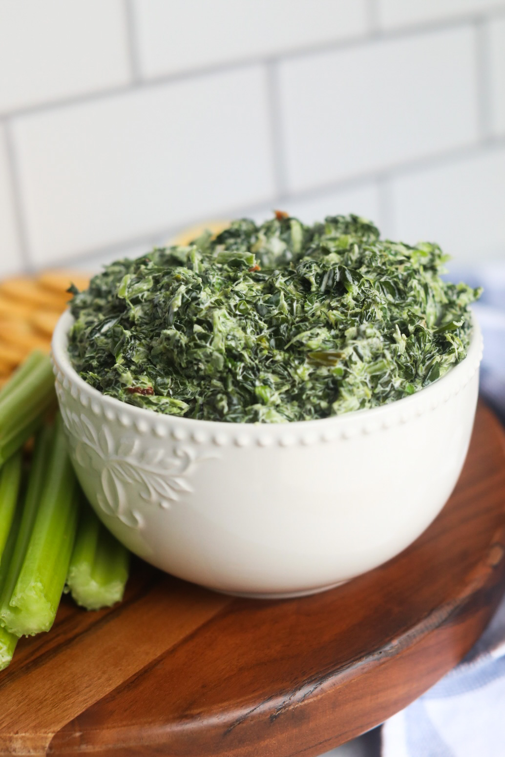 Final recipe, cold spinach dip in a white bowl with celery, carrots and crackers.