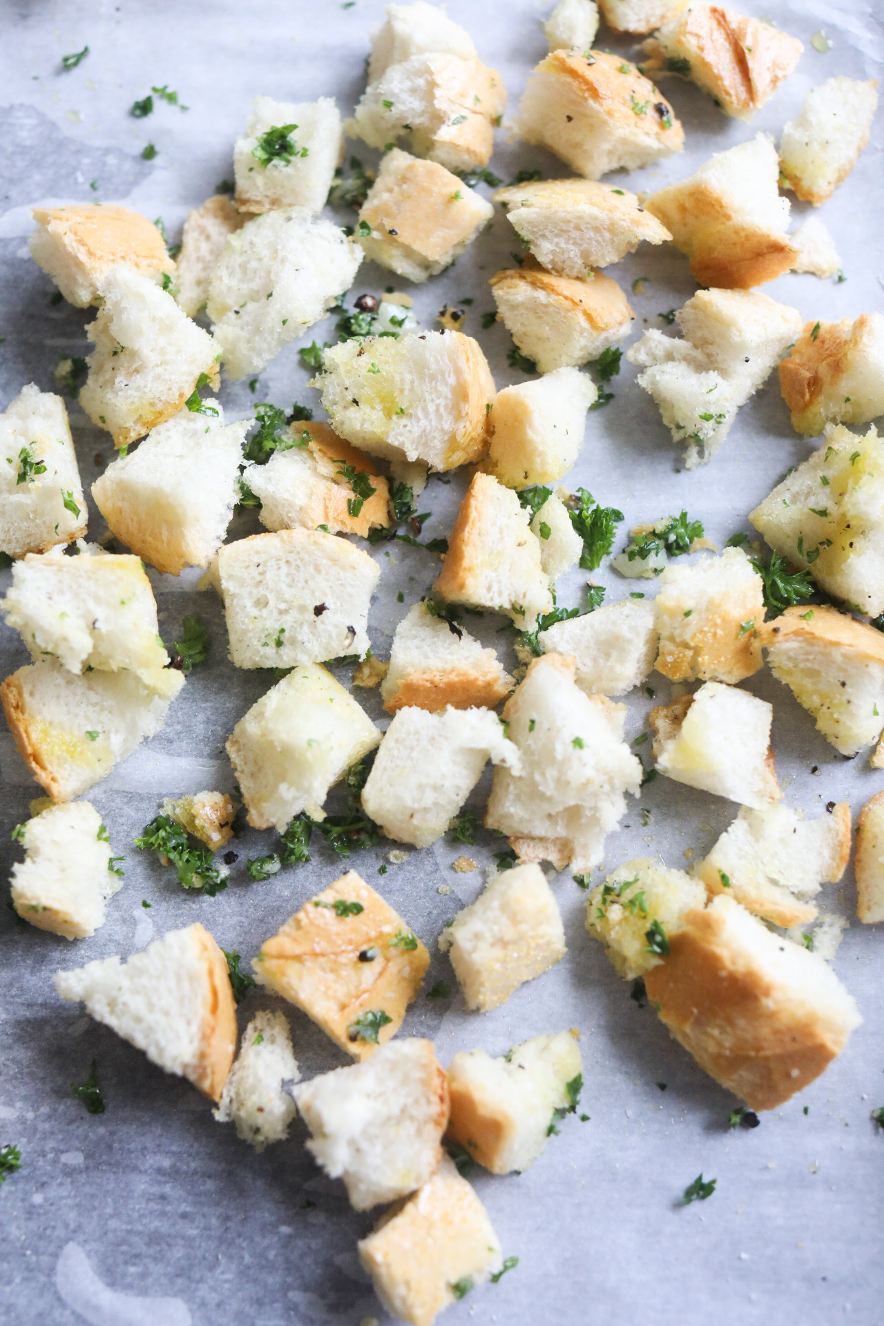 Homemade croutons on a lined baking sheet with olive oil, seasonings and herbs before being baked.
