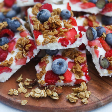 Yogurt bark cut into squares served on a wooden board. On top of frozen greek yogurt are mixed berries and granola.