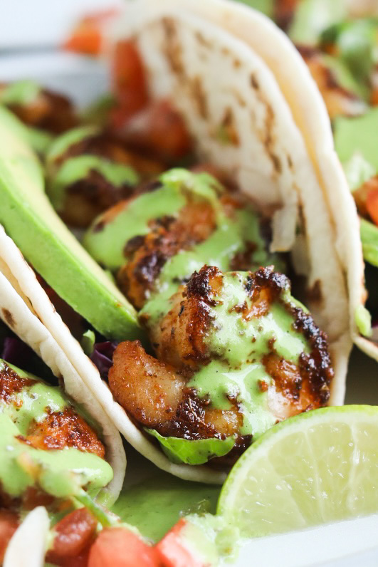Blackened Shrimp Tacos with Cilantro Lime Sauce plated and zoomed in to show charred shrimp and sauce drizzle.